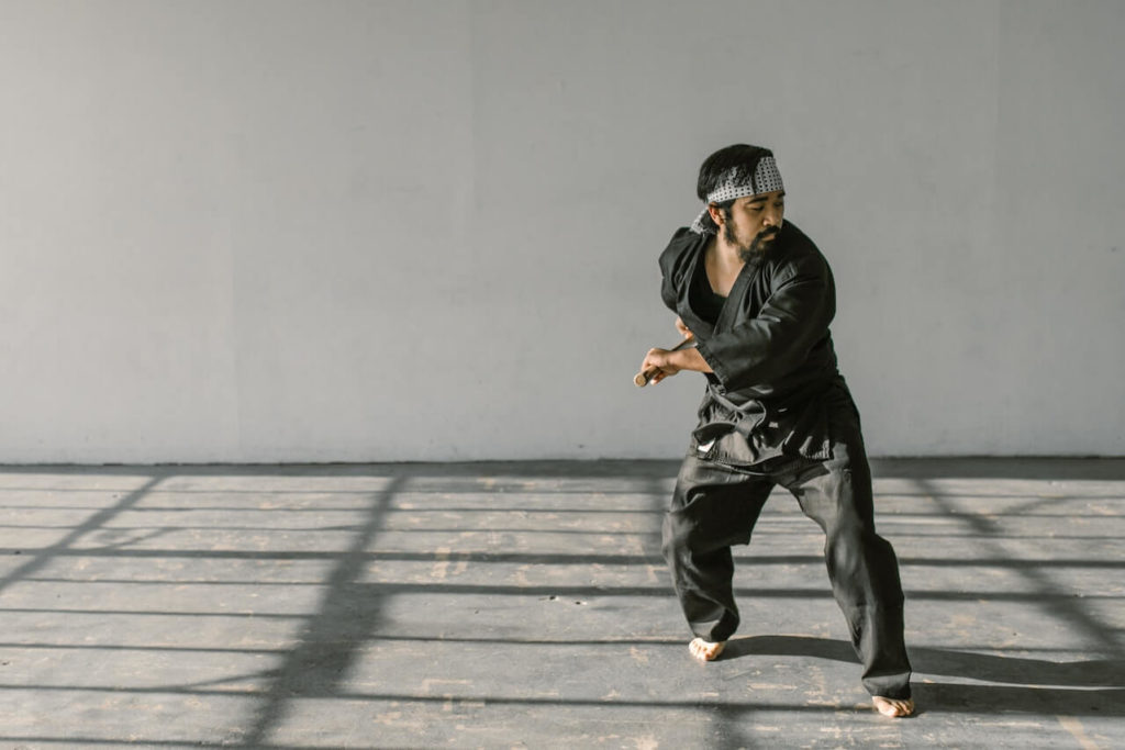 Build discipline through habits: A man practicing his martial arts stance in a courtyard, wearing a black gi and white headband.