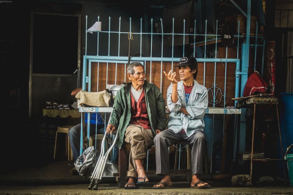 Two elderly Asian men sat outside of a store having interesting conversations.